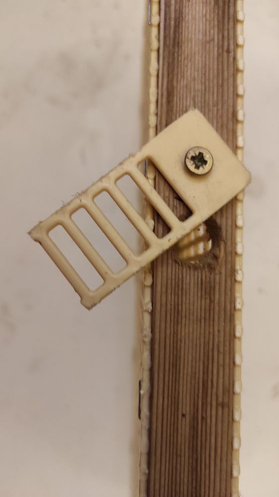 Gros plan sur la latte supérieure du cadre : le trou de 12 mm par lequel on introduit la reine, fermé par un clapet pivotant fixé par une vis.